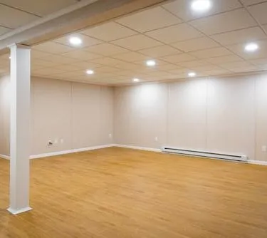 Finished basement room with hardwood flooring, support columns, and recessed lighting