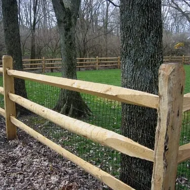 Three-rail wood fence with wire liner running through a wooded yard
