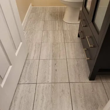 Light tile flooring installed beside a bathroom vanity and toilet