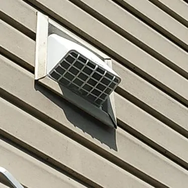 Exterior vent cover installed on light-colored house siding