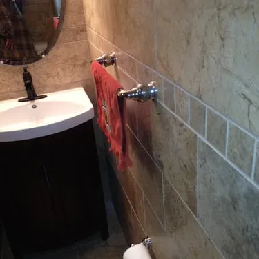 Tiled bathroom wall beside a sink and exposed plumbing