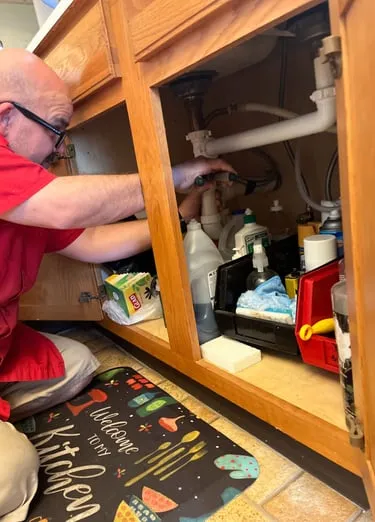 Kirk Metz working beneath a kitchen sink during a repair